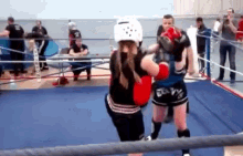 two young girls are boxing in a ring and one of them is wearing a helmet that says boxing on it .