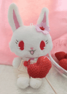 a stuffed bunny with red eyes is holding a heart shaped strawberry