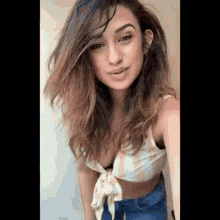 a woman is wearing a striped crop top and jeans and taking a selfie .