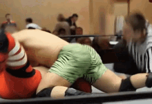 two men are wrestling in a ring and one has green shorts on