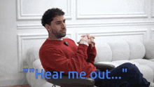 a man in a red sweater sits in a chair with the words " hear me out " above him