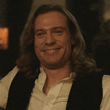 a man with long hair is smiling and wearing a white shirt