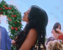 a woman with long black hair is standing in front of a floral arch