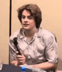 a man is sitting at a table holding a microphone and talking into it .