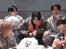 a group of young men are sitting around a table with a stuffed animal and a cell phone .