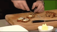 a person is cutting bread with butter on it on a cutting board .