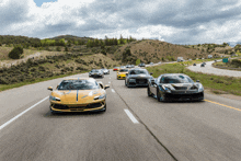 a row of sports cars are driving down a highway with mountains in the background