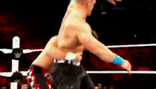 two men are wrestling in a wrestling ring and one of them is without a shirt on .