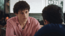 a man in a pink and white striped shirt talks to another man
