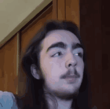 a young man with long hair and a beard is looking at the camera and making a funny face .