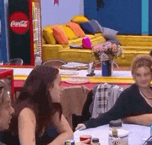 a group of people are sitting at a table with a coca cola fridge in the background