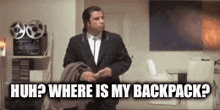 a man in a suit and tie is standing in a room and asking where is his backpack