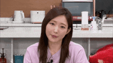 a woman in a pink shirt stands in front of a counter with a microwave and a bottle of hand sanitizer on it