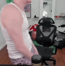 a man in a white tank top is standing in front of a computer chair .