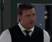 a man wearing a vest and tie is standing in front of a door .