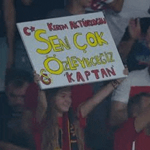 a woman is holding a sign in a crowd of people at a stadium .