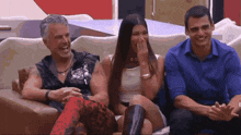 three people are sitting on a couch laughing and one of them is covering her mouth