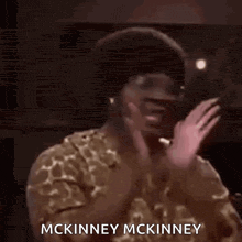 a man wearing glasses and a giraffe print shirt is saying mckinney mckinney in a dark room .