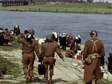 a group of soldiers are walking by a river with the words kronos media on the bottom right