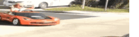 a little boy is driving a red toy car on a street