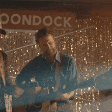 a man playing a guitar in front of a sign that says " oondock "