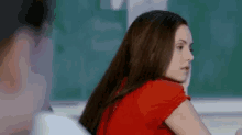a woman in a red shirt is sitting in a classroom next to a man .