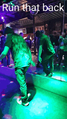 a man in a green shirt is dancing in front of a mirror with the words run that back below him