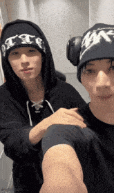 two young men are posing for a picture and one of them is wearing a hoodie and headphones .