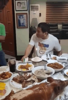 a man is sitting at a table with plates of food and a pig on the table