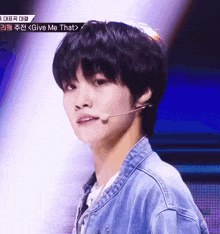 a young man wearing a denim jacket stands in front of a microphone with the words give me that on the bottom