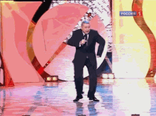 a man in a suit and tie stands on a stage with a microphone and a sign that says " russia "