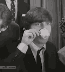 a man in a suit and tie is drinking from a white cup .