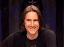 a man wearing a black shirt with the letter t on it smiles