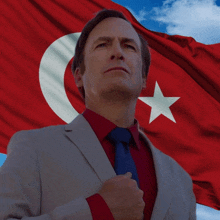 a man in a suit and tie is standing in front of a red and white flag