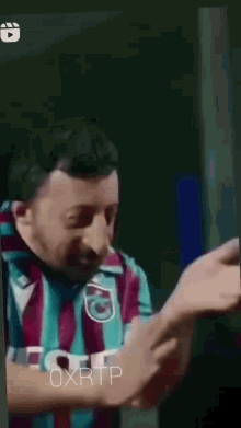 a man with a beard is wearing a striped shirt and scarf and making a funny face .