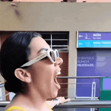 a woman wearing sunglasses yawning in front of a sign that says saida