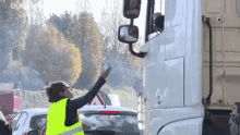 a woman in a yellow vest is pointing at a truck