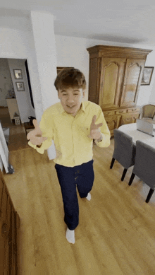 a man in a yellow shirt and blue pants is dancing in a living room