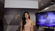 a woman stands in front of a samsung qled 8 television