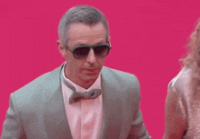 a man in a suit and bow tie is standing on a pink carpet