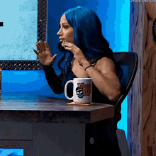 a woman with blue hair is sitting at a table with a mug that says " broken skin " on it