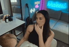 a woman sitting in front of a khaleesi neon sign