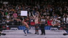 a wrestler is holding a sign that says aew in front of a crowd .