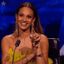 a woman in a yellow dress is smiling in front of a microphone with a star in the background