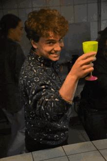 a young man holds up a yellow cup in his hand
