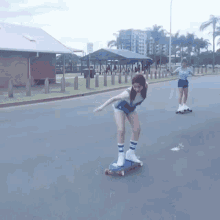 a woman is riding a skateboard down a street while another woman looks on ..