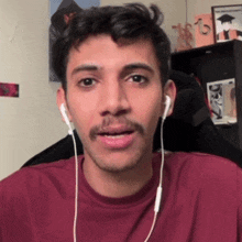 a man with a mustache wearing ear buds and a maroon shirt