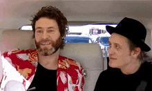two men are sitting in the back seat of a car and one of them is wearing a hat