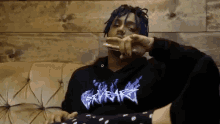 a man with blue dreadlocks is sitting on a couch smoking a cigarette
