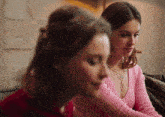 a woman in a pink sweater sits next to another woman in a red shirt